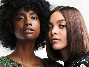 Two women posing closely, one with curly hair and the other with straight hair, looking directly at the camera, showcase stunning results from top-notch hair services in Annapolis, MD.