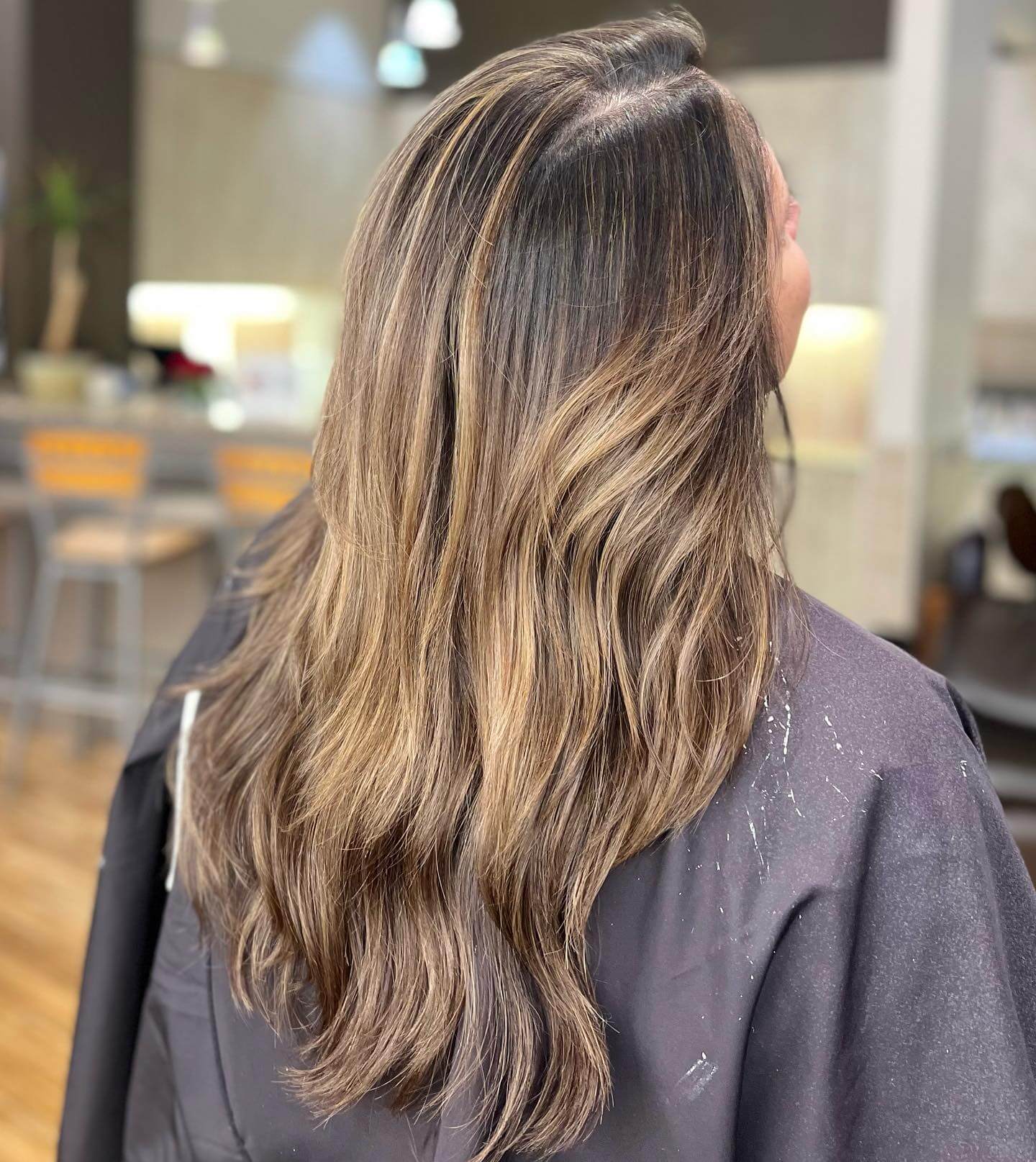 A person with long, wavy, highlighted hair is photographed from the back in a chic hair salon downtown Annapolis. - Varuna Salon Spa in Annapolis, MD