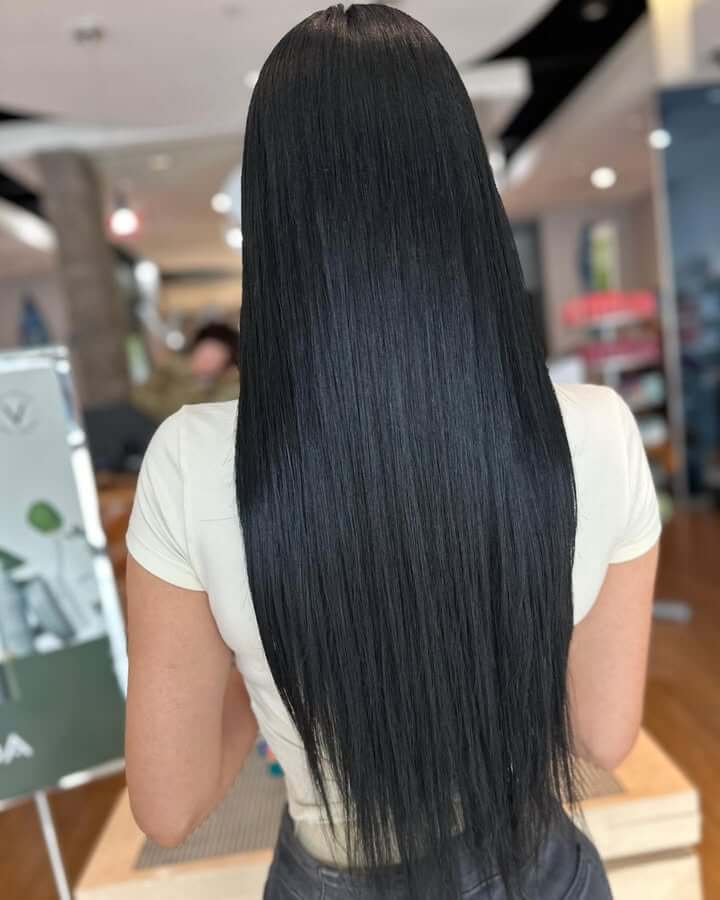 A person with long, straight, black hair is seen from behind, standing indoors in a short-sleeved light-colored shirt—perhaps waiting for a pampering session at the best salon Annapolis MD has to offer. - Varuna Salon Spa in Annapolis, MD